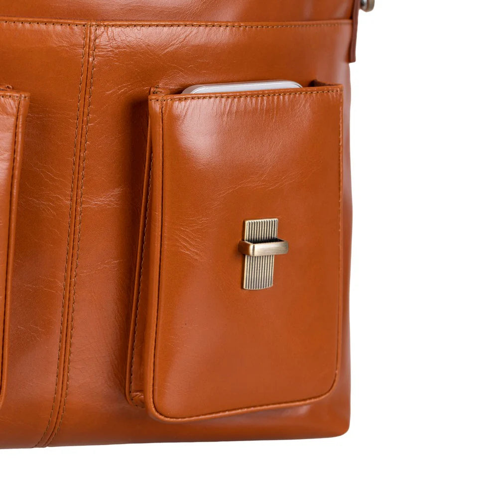Close-up of a brown leather bag showing a front slip pocket with a gold-tone metal clasp and a phone partially tucked inside.