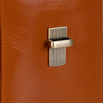Close-up of a rectangular brass-toned metal latch or clasp mounted on a warm brown leather surface.