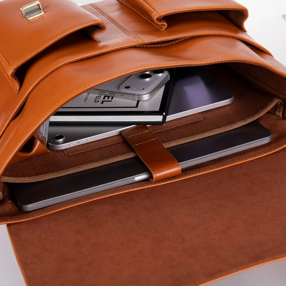 A close-up of a brown leather messenger bag shown open, with a smartphone, tablet, and notebook tucked inside the compartment.
