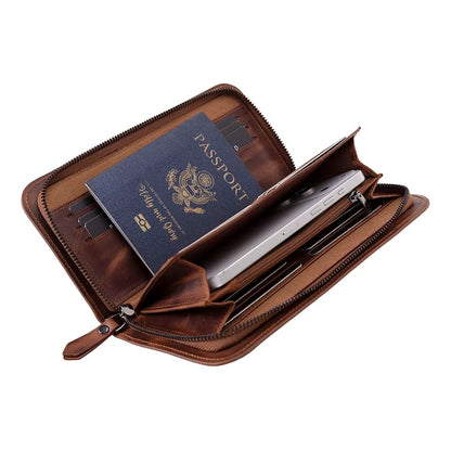A brown leather passport holder and document case shown open, containing a blue passport, a silver tablet, and card slots, on a plain white background.