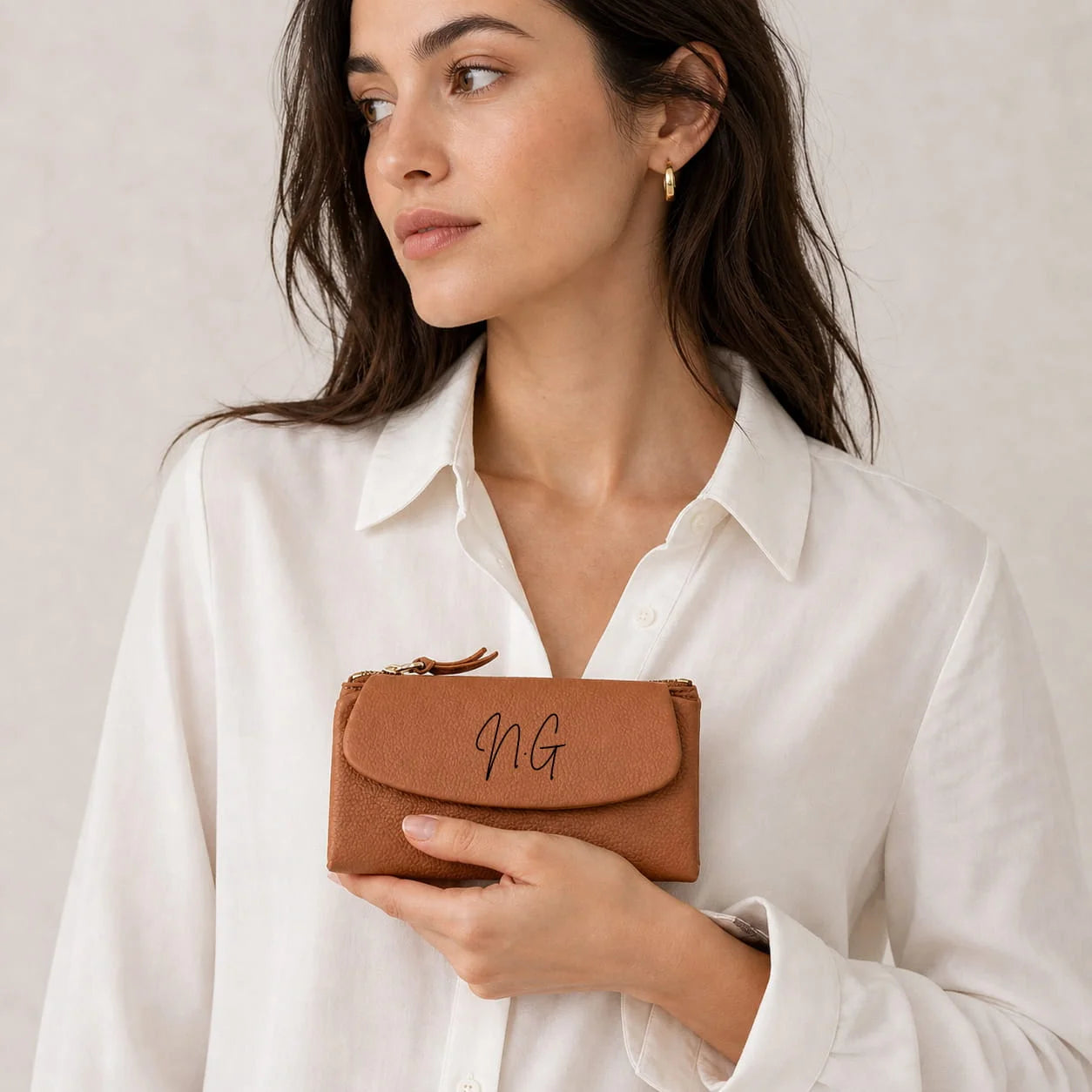 Woman holding a brown leather wallet with initials 'NG' on a plain background